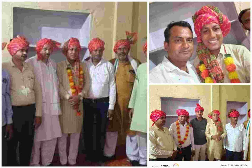कई पुरुष पारंपरिक राजस्थानी साफा और माला पहनकर दीवार के सामने समूह में खड़े हैं