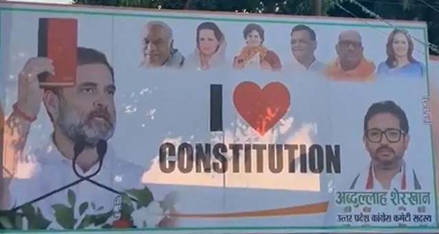 सड़क किनारे लगा एक पोस्टर जिसमें "I ♥ Constitution" लिखा है और कई लोगों के चेहरे धुंधले दिखाए गए हैं।