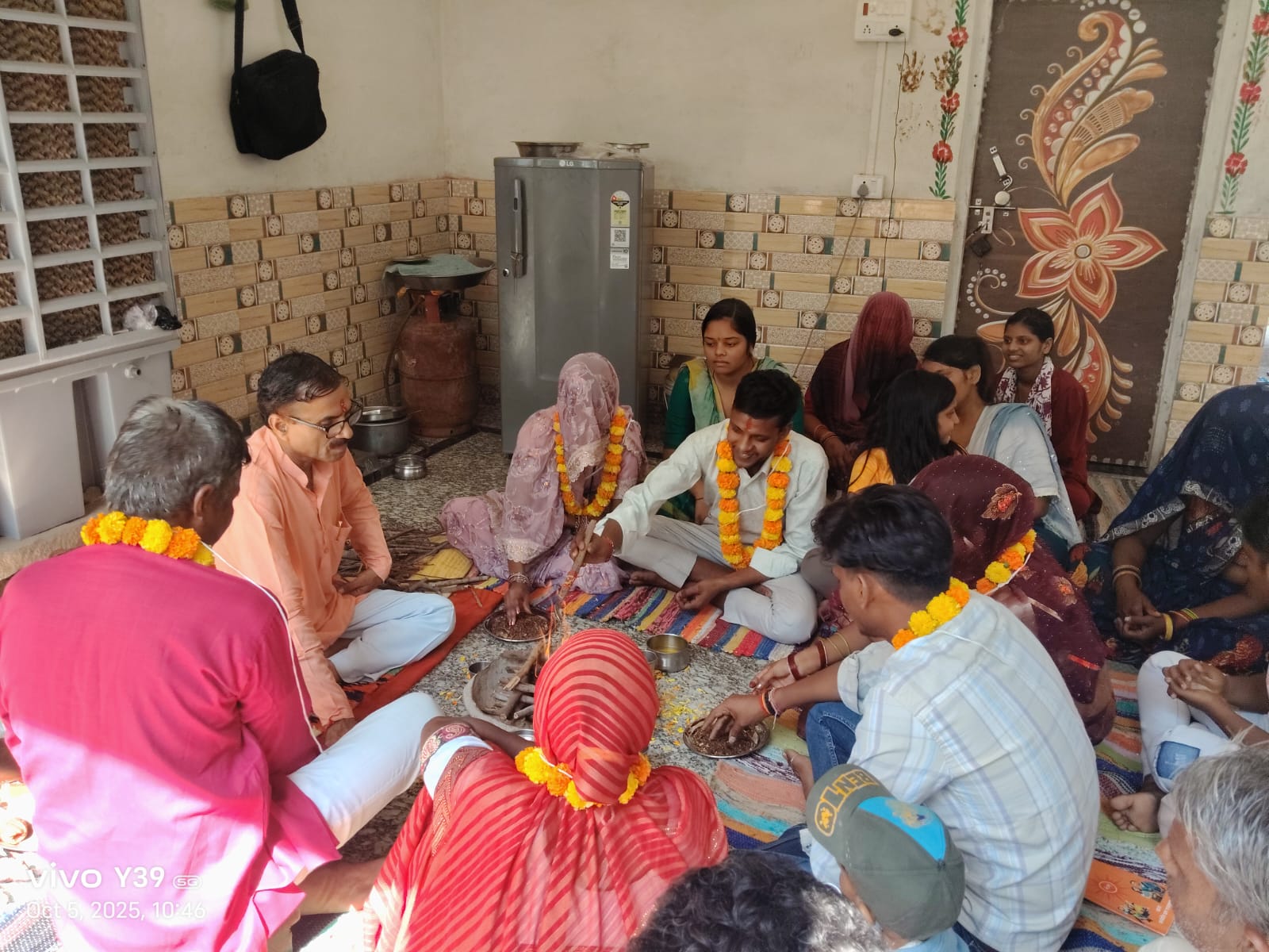 एक घर के अंदर हवन के दौरान पुरोहित और परिवार के सदस्य पूजा करते हुए, सभी ने गेंदा माला पहन रखी है और पूजा सामग्री आस-पास रखी है।