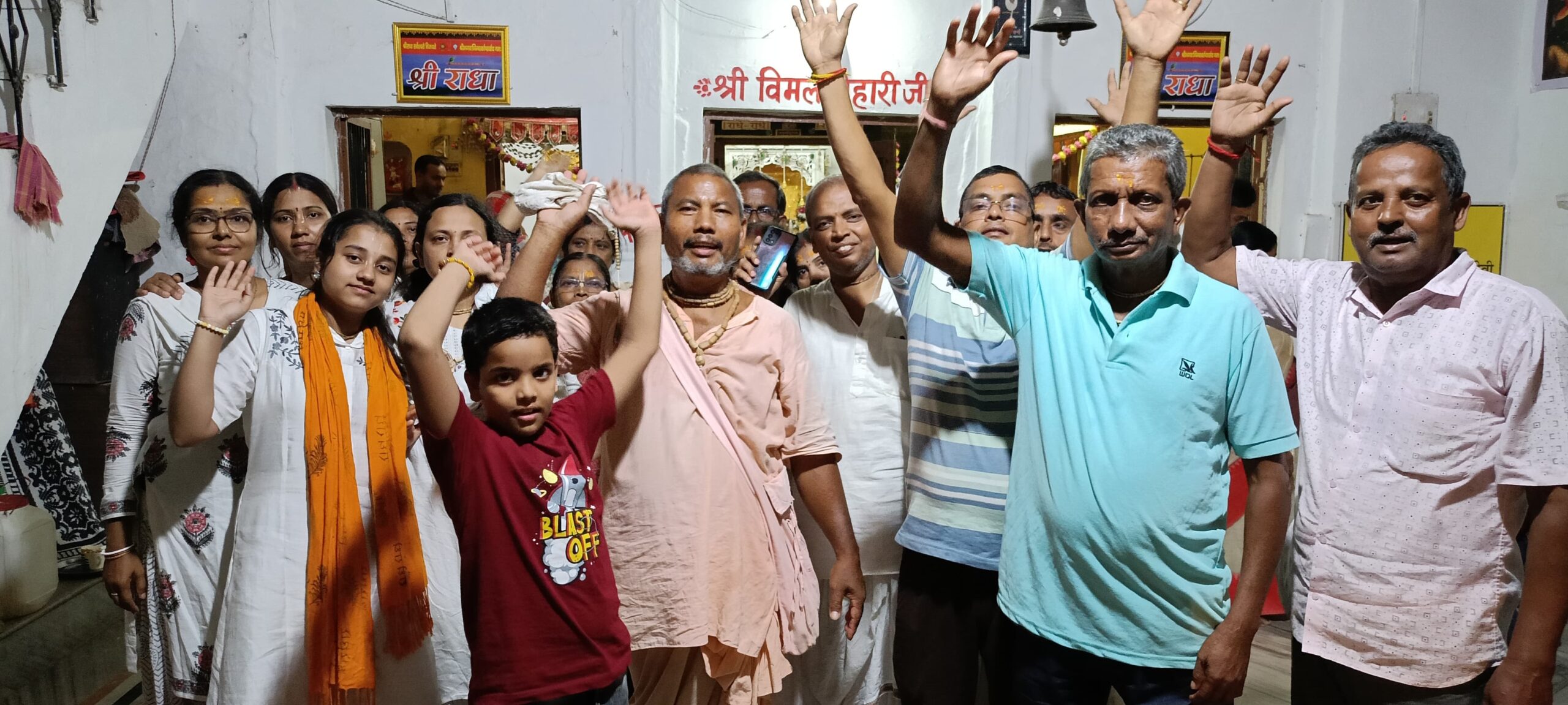 एक भीड़ जिसमें महिलाएं, पुरुष और बच्चे पारंपरिक कपड़ों में धार्मिक स्थल के बाहर खड़े हैं