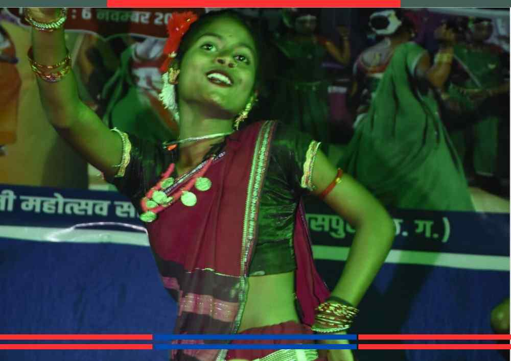 छत्तीसगढ़ की एक युवती पारंपरिक साड़ी और आभूषण पहनकर मंच पर सुआ नृत्य प्रस्तुत करती हुई, सामने प्रतीकात्मक तोते की आकृतियाँ रखी हैं।