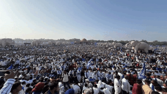 "खुले मैदान में हजारों लोगों की भीड़, चारों ओर हाथी की मूर्तियां, नीला आसमान और दूर तक फैली सभा।"