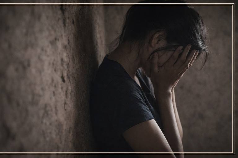 अंधेरी दीवार के सहारे खड़ी एक युवती की सिल्हूट, चेहरा ढका हुआ, भावनात्मक पीड़ा का प्रतीकात्मक दृश्य